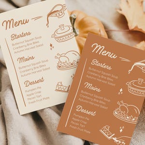May include: Two menu cards with a fall theme. One card is beige, the other is brown. Both cards have the word "Menu" at the top, followed by "Starters", "Mains", and "Dessert". The menu items are listed below each heading. Decorative illustrations of food are also present.