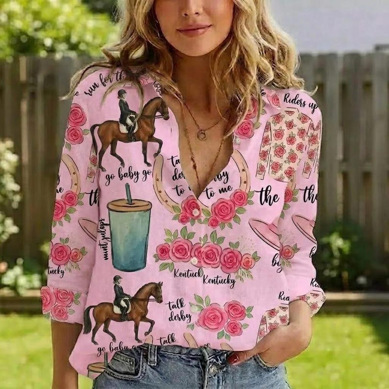 May include: A light pink long-sleeve button-down shirt featuring a repeating pattern of horses with riders, mint julep cups, horseshoes, and pink roses. The shirt includes cursive text that reads "run for the roses," "riders up," and "Kentucky."