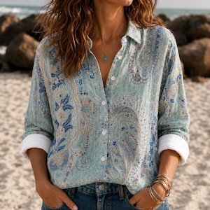 Puede incluir: Una camisa de manga larga con botones que presenta un estampado de cachemira en azul claro y blanco con detalles florales. La camisa tiene un cuello clásico, una tapeta de botones frontal y puños blancos remangados hasta el antebrazo.