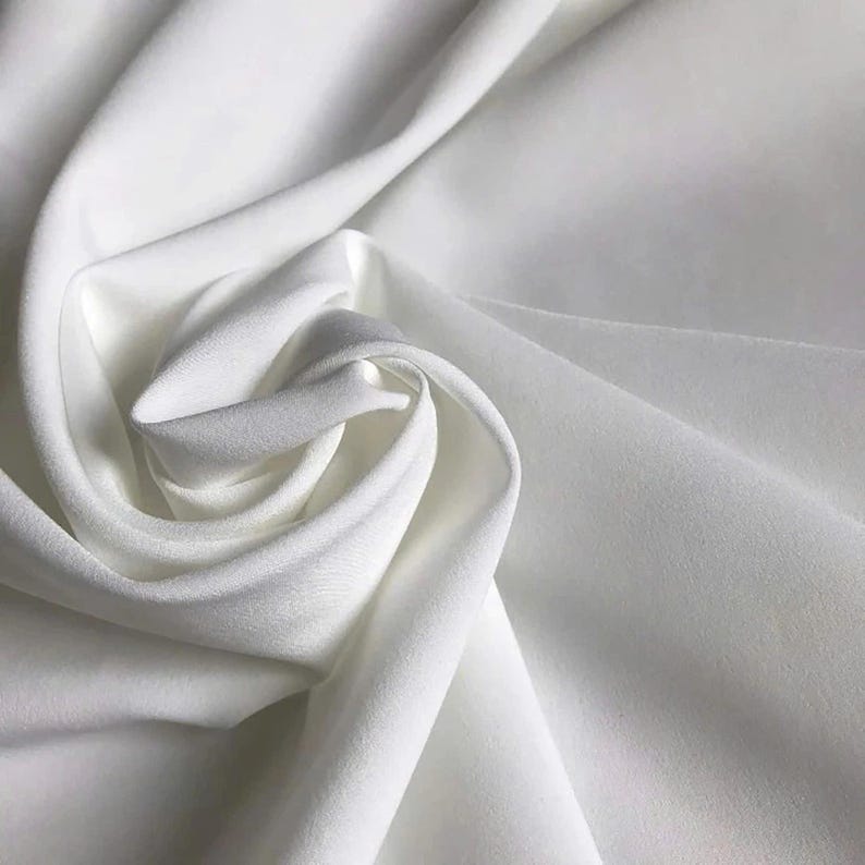 May include: A solid white fabric with a smooth, matte texture, draped in soft, flowing folds that create deep shadows and highlights. The material appears opaque and consistent in colour, forming a swirling, circular pattern in the centre.