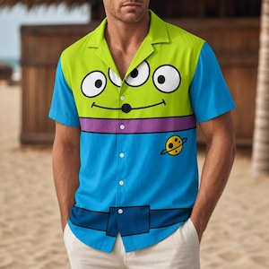 May include: A short-sleeve button-down shirt featuring a lime green top section with three large white eyes and a black smile. The midsection is purple, and the bottom is blue with a yellow planet graphic and a dark blue belt design at the hem.