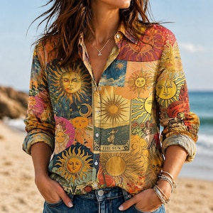 Op de afbeelding: Een button-down shirt met lange mouwen en een kleurrijk zonontwerp. Het shirt toont verschillende zonillustraties in tinten geel, oranje en blauw, met de tekst "THE SUN" zichtbaar. Het shirt wordt gecombineerd met een blauwe jeans.