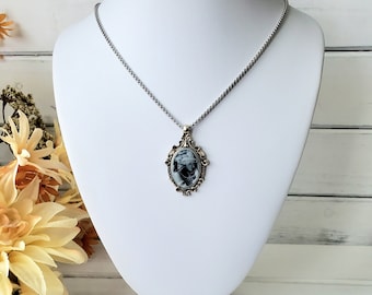 May include: A silver chain necklace with a cameo pendant. The cameo is oval shaped and features a black and white image of a woman's face. The pendant is set in a gold-toned frame with ornate details.