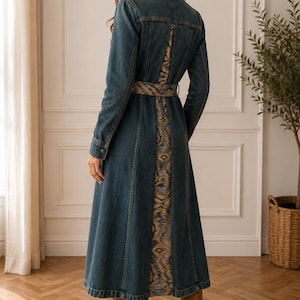 May include: A long-sleeved denim coat dress in a dark blue wash, featuring a structured collar, buttoned cuffs, and a matching fabric belt. The back panel and belt are accented with a vertical, multi-coloured ikat-style patterned fabric insert.