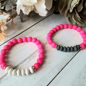 May include: Two lava rock beaded bracelets. One bracelet is pink and white, the other is black and pink.