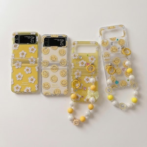 以下が含まれることがあります： スマイリーフェイスとデイジー柄など、様々なデザインの黄色の携帯電話ケース4つ。1つのケースには、黄色と白のビーズが付いたビーズストラップが付いています。ケースは透明で、携帯電話のデザインが見えるようになっています。