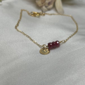 May include: A gold chain bracelet with a small gold charm and a row of red gemstone beads.