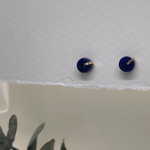 May include: A pair of small, round, dark blue earrings with gold accents. The earrings are on a white surface.