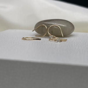 May include: A set of three gold earrings with small clear stones. The earrings are on a white surface.