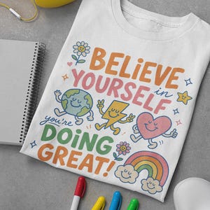 Puede incluir: Una camiseta blanca con un gráfico colorido que incluye el texto BELIEVE IN YOURSELF you're DOING GREAT! El diseño presenta una tierra sonriente, un rayo, un corazón, un arcoíris con nubes y flores en tonos naranja, rosa, azul y verde.