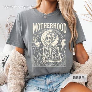 May include: Grey t-shirt with the word "MOTHERHOOD" above a skeleton graphic. The graphic includes a butterfly, a planet, a lightning bolt, and the text "SOME DAYS I ROCK IT - SOME DAYS IT ROCKS ME". The text "EITHER WAY WE'RE ROCK" is also included.