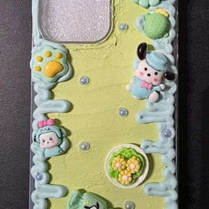 May include: A decorative phone case with a light green textured background and light blue trim. The case features various 3D embellishments, including a smiling flower, a cactus, and several cartoon characters. The text "Option #2" is at the top.