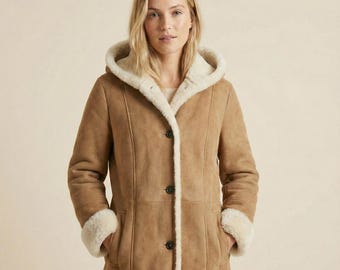May include: A tan-colored coat with a hood and a cream-colored lining. The coat has a button-up front, pockets, and cream-colored trim on the cuffs and around the hood. The coat appears to be made of suede or a similar material.