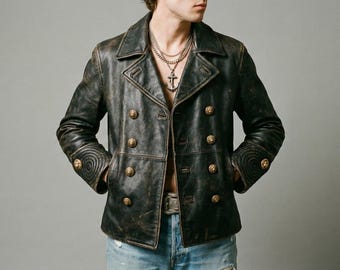 May include: A distressed dark brown leather pea coat featuring a double-breasted front with gold-toned buttons, wide lapels, and circular stitched detailing on the cuffs. The jacket is worn open over blue denim jeans and a silver anchor necklace.