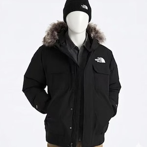 Peut inclure: Veste d'hiver noire avec capuche bordée de fourrure et bonnet noir assorti. La veste porte le logo blanc "The North Face" sur la poitrine et la poche. La veste a une fermeture boutonnée et deux poches avant.