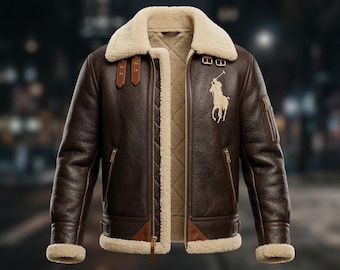 May include: A brown leather jacket with a cream-colored shearling collar and lining. The jacket features a zip closure, two front pockets, and a tan embroidered logo of a polo player on the chest. The jacket has brown leather straps and buckles.