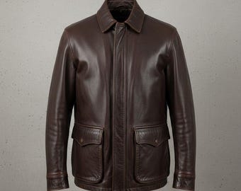May include: A brown leather jacket with a collared neckline and two front pockets. The jacket has a classic design with a button closure and a smooth, polished finish. The jacket is a medium brown color.