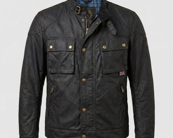 May include: Black waxed cotton jacket with a stand-up collar, multiple pockets, and a zipper closure. Features gold-colored buttons and a small Union Jack flag patch. The jacket has a classic, rugged design.