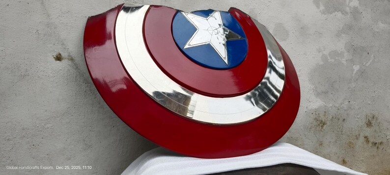 May include: A red, white, blue, and silver shield with a star emblem. The shield has a circular design with concentric rings of colour. The central emblem is a white star on a blue background. The shield is a prop or collectible.