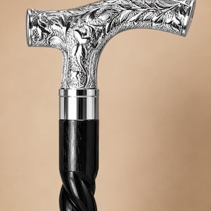 Op de afbeelding: Een wandelstok met een zilverkleurig handvat voorzien van een gedetailleerd bloemmotief in reli&euml;f. Het handvat is verbonden met een gladde, zwarte houten schacht die onder de gepolijste zilveren kraag overgaat in een gedraaid spiraalontwerp.