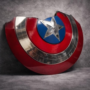 May include: A damaged Captain America shield. The shield has a red and silver design with a blue centre and a silver star. It is leaning against a grey textured surface, showcasing its iconic design.