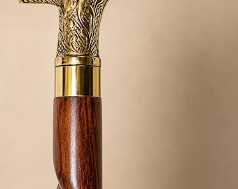 May include: A walking stick featuring a polished brass T-shaped handle with intricate embossed floral and cross-hatched patterns. The handle connects to a dark brown wooden shaft that displays a distinct spiral or twisted design along its length.