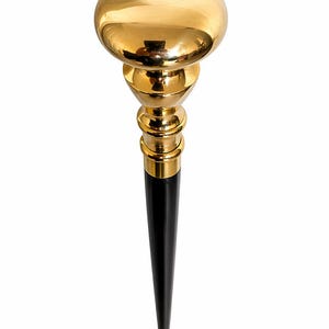 Puede incluir: Un tapón de botella decorativo con una parte superior redondeada de color dorado y una base puntiaguda negra. El tapón tiene una sección media dorada con una serie de detalles redondeados. El diseño es elegante y sería una buena adición a una colección de bar o vino.