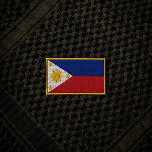 May include: A rectangular patch featuring the flag of the Philippines, with a blue upper section, a red lower section, and a white triangle containing a sun and stars. The patch is set against a dark green and black houndstooth pattern.