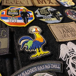 May include: A collection of embroidered patches, including military-themed designs and a colorful rooster. Patches feature text like "HANA HOU", "HONEY BADGER HAS NO CHILL", and "UNITED STATES MILITARY".
