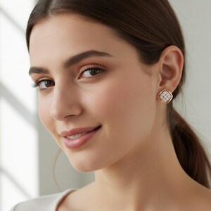 Puede incluir: Pendientes cuadrados de oro rosa con un centro agrupado similar a un diamante. Los pendientes tienen un marco cuadrado con un acabado en oro rosa y un grupo de pequeñas piedras transparentes en el centro.