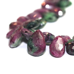 May include: A strand of faceted teardrop-shaped gemstone beads. The beads are a mix of pink and green, with a pearlescent sheen.