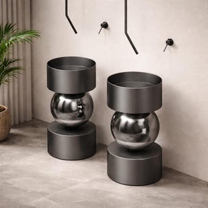 Peut inclure: Deux lavabos sur pied modernes gris foncé. Ils présentent une base cylindrique, une sphère centrale et un dessus circulaire. Ils sont placés devant un mur clair avec des accessoires noirs.