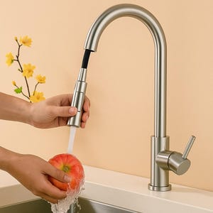 Może przedstawiać: Bateria kuchenna ze szczotkowanego niklu z wysoką wylewką i wyciąganym spryskiwaczem. Bateria jest pokazana z wodą rozpryskującą się na czerwonym jabłku. Bateria ma pojedynczy uchwyt dźwigniowy.