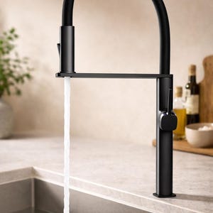 May include: A modern black kitchen faucet with a high arc spout. Water flows from the faucet into a stainless steel sink. The faucet has a single lever handle and a sleek, minimalist design. The faucet is mounted on a light-colored countertop.