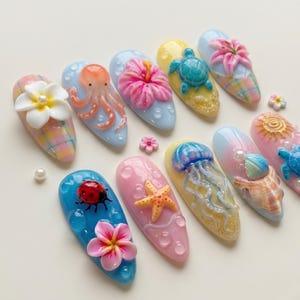 May include: A collection of ten artificial nails with various 3D designs. The designs include a white flower, an octopus, a pink hibiscus, a blue turtle, a ladybug, a starfish, a jellyfish, a seashell, and a sun. The nails are painted in pastel colors.