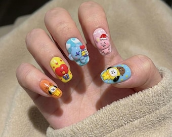 May include: A hand displaying five acrylic nails, each with a different cartoon character design. The nails feature characters in various colors, including yellow, blue, orange, and pink, with detailed 3D elements. The nail art is set against a neutral background.
