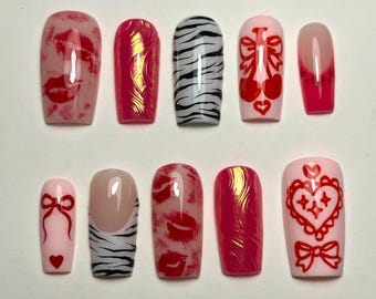 May include: A set of ten artificial nails in various designs. The nails feature patterns such as red lips, zebra stripes, bows, and hearts. Colors include pink, red, and white. The nails are rectangular in shape.