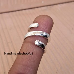 May include: A silver spiral ring with an open design. The ring wraps around a finger, displaying its smooth, reflective surface. The text "HandmaadeshopArt" is visible in the image.