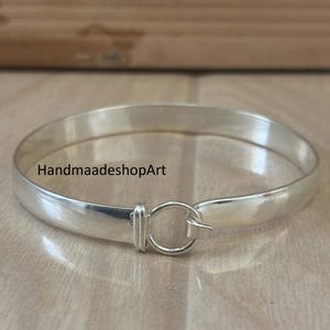 Peut inclure: Un bracelet jonc argenté avec une fermeture à fermoir. Le bracelet a une finition lisse et polie et un design simple. Le texte "HandmaadeshopArt" est imprimé sur le bracelet.
