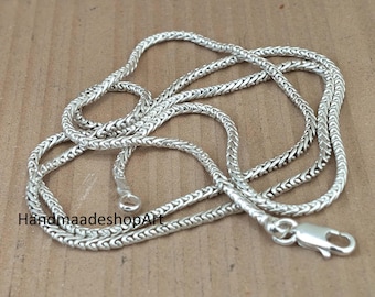 Può includere: Una collana a catena color argento con un design intrecciato. La collana è appoggiata su una superficie marrone. La chiusura e l'asola finale sono visibili. Il testo "HandmaadeshopArt" è visibile in basso a sinistra.