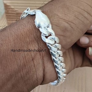 Könnte beinhalten: Ein silbernes Panzerkettenarmband mit sicherem Verschluss. Das Armband wird am Handgelenk getragen und zeigt seine polierten Glieder und sein Design. Der Text "HandmaadeshopArt" ist sichtbar.