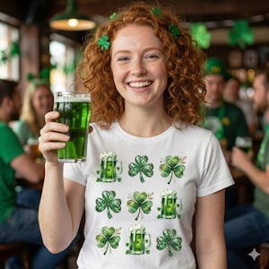 May include: A white t-shirt with a pattern of green shamrocks and green beer mugs. The person in the image is holding a pint of green beer and wearing shamrock hair clips. The background shows a pub setting.