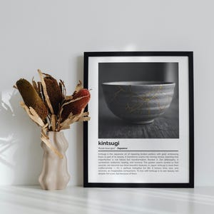 K&ouml;nnte beinhalten: Ein schwarz gerahmter Druck mit einem Graustufenbild einer japanischen Kintsugi-Schale mit goldenen Akzenten. Daneben steht eine beige Vase mit getrockneten Blumen. Der Text "kintsugi" ist sichtbar.