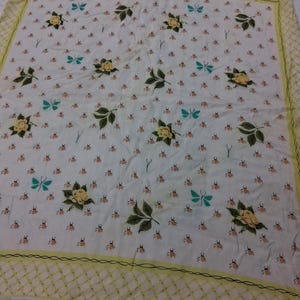 May include: A square, white scarf with a repeating pattern of small orange bugs, teal butterflies, and yellow roses with green leaves. The border is a yellow lattice design with a black outline.