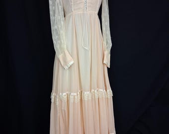 May include: A vintage peach-colored maxi dress with long, sheer lace sleeves. The dress features a scoop neckline, a bodice with a drawstring, and tiered skirt with lace and ribbon trim. The dress is displayed on a mannequin.