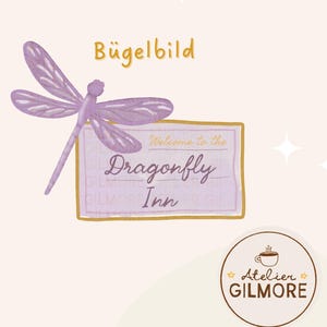 Puede incluir: Un diseño de libélula lavanda con el texto "Welcome to the Dragonfly Inn" sobre un fondo morado claro. La imagen también incluye el texto "Bügelbild" y un logotipo circular con una taza de café.