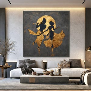 May include: A square wall art piece featuring a dark grey textured background with a large gold circular moon. Two silhouettes of figures are depicted in gold, with one figure playing a flute and the other dancing, both wearing flowing garments.