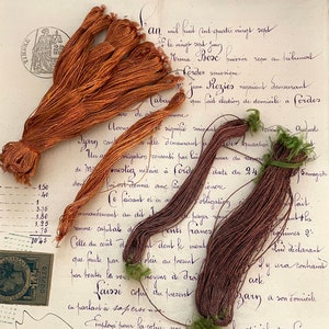 May include: A close-up of a document with handwritten text in French. The document is dated 1887 and includes a handwritten signature. There are also several spools of brown and green thread.