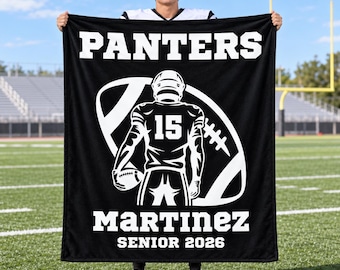 May include: A black fleece blanket featuring a white graphic of a football player wearing jersey number 15, centred over a football outline. The text reads PANTERS, MARTINEZ, and SENIOR 2026 in bold white lettering across the top and bottom.