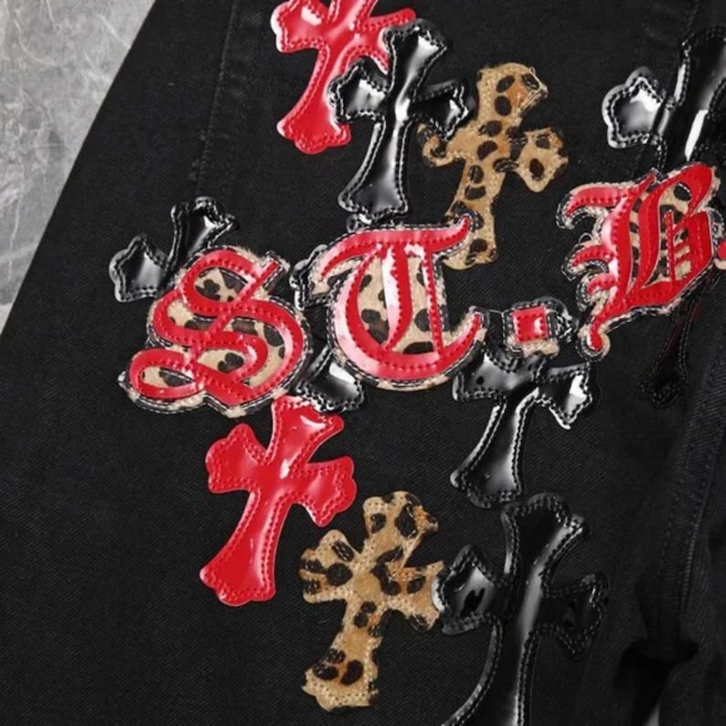 Puede incluir: Tejido negro con parches decorativos. Los parches incluyen cruces rojas, negras y con estampado de leopardo y letras estilizadas. Los parches est&aacute;n cosidos a la tela.